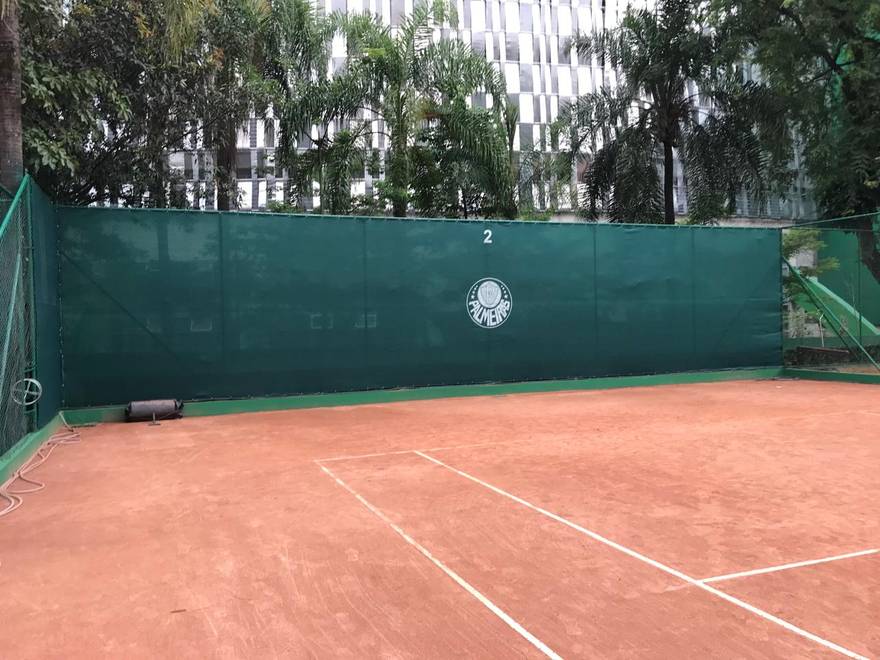 Quadra de saibro com tela de fechamento verde e o escudo do Palmeiras aplicado.
