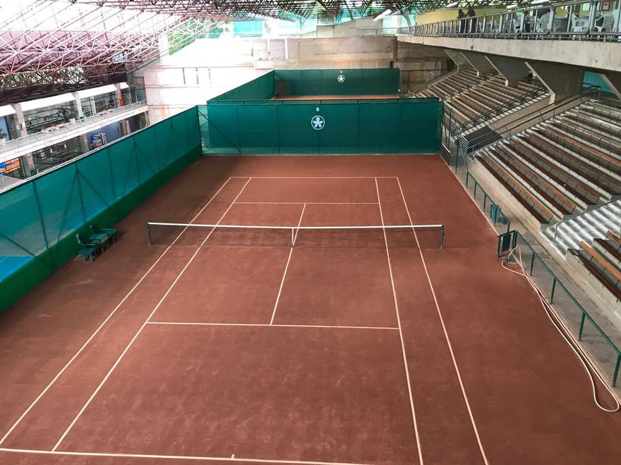 Quadra coberta com arquibancada, tela de fechamento e logo do clube nas laterais.