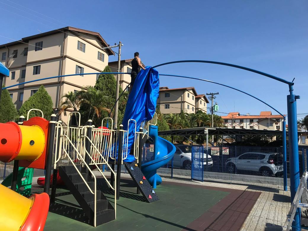Instalação da cobertura sobre a estrutura do playground, tela sendo fixada no arco